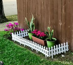 a white picket fence with potted plants on the top and flowers in the bottom