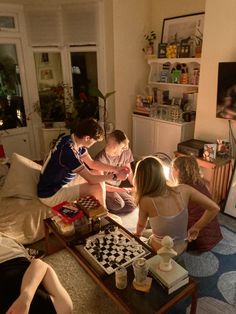 four people sitting on a couch in a living room playing checkers and chess together