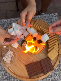 two hands reaching for marshmallows on a plate with chocolate and marshmallows