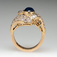 This elegant ring is centered with one (1), bezel set, oval cabochon cut natural sapphire. The sapphire is bordered with eight (8), channel set, tapered baguette cut diamonds and thirty-two (32), bead set, round brilliant cut diamonds. The ring measures 17.0mm at the top, rises 9.7mm above the finger, tapering to 3.8mm wide and 2.0mm thick at the base of the shank. This ring is currently a size 6. Formal Oval Cabochon Sapphire Ring, Classic Cabochon Sapphire Ring For Formal Occasions, Classic Formal Cabochon Sapphire Ring, Classic Formal Sapphire Cabochon Ring, Formal Polished Finish Oval Cabochon Sapphire Ring, Luxury Cabochon Diamond Ring For Formal Occasions, Luxury Sapphire Cabochon Ring, Elegant Sapphire Cabochon Rings, Luxury Formal Cabochon Diamond Ring