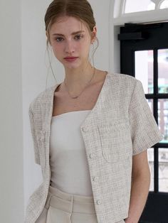 This product is a sophisticated blouse crafted in a tweed fabric, offering both texture and a touch of elegance to the wearer. The piece features a classic collar and is adorned with a set of coordinating buttons, providing a seamless look that is perfect for professional settings or everyday chic. Its short sleeves and tailored fit bring a modern twist to the traditional tweed aesthetic. - The blouse’s tailored fit accentuates the body's silhouette while maintaining a comfortable range of movement.- Short sleeves add a contemporary and casual element to the otherwise formal tweed fabric.- Coordinating buttons down the front lend a cohesive and polished finish to the design.- The classic collar rounds off the blouse's design, making it a versatile piece that can be dressed up or Spring Elegant Tweed Jacket With Hidden Buttons, Chic Spring Semi-formal Tweed Jacket, Elegant Beige Tweed Jacket For Spring, Chic Beige Tweed Jacket For Office, Spring Classic Tweed Jacket For Office, Classic Spring Tweed Jacket For Office Wear, Classic Spring Tweed Office Jacket, Elegant Spring Button-up Tweed Jacket, Elegant Spring Tweed Button-up Jacket