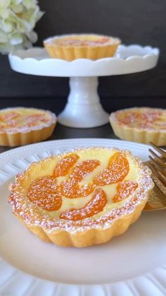 an orange tart with powdered sugar on top and other desserts in the background