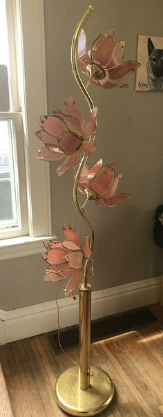 a metal sculpture with pink flowers sitting on top of a wooden floor next to a window