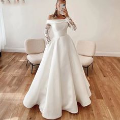 a woman taking a selfie wearing a white wedding dress with long sleeves and an off - the - shoulder neckline