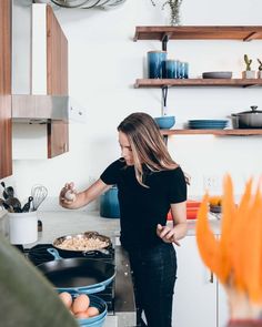 a woman standing in a kitchen next to a stove top oven with eggs on it