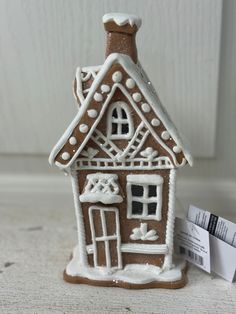 a small gingerbread house with snow on the roof and windows is next to a business card holder