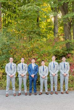 a group of men standing next to each other in front of trees and bushes with one man wearing a blue suit