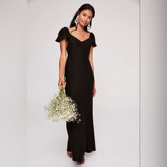 a woman in a long black dress holding a bouquet of white flowers and wearing earrings