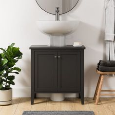 a white sink sitting under a mirror next to a wooden stool and potted plant