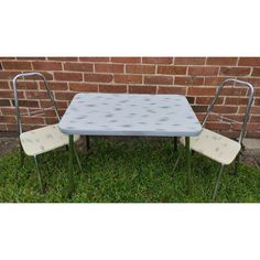 a table and two chairs sitting in front of a brick wall with grass on the ground