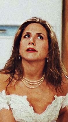 a woman in a white dress with pearls on her neck looking up to the sky