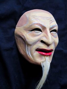 an old man's mask with long white hair and red lips on a black background