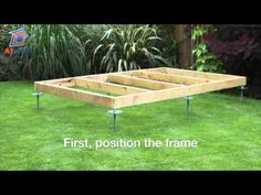 a wooden bed frame sitting in the middle of a grass covered yard with metal legs