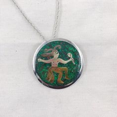 This vintage Mexican Silver piece functions as both a pendant and a brooch.  The piece features a green background with married metal overlay to create a figure in traditional dress.  This pendant comes with a 24" sterling silver wheat chain and is in good vintage condition.Stamps: Metales casadas (married metals) Mexico 925 Sterling Taxco Diameter: 68 mm/2 1/8 inchChain: 24 inch wheat styleThese pieces are pre-owned vintage jewelry. As this jewelry is not new there may be signs of wear or age. Green Engraved Necklace For Collectors, Green Medallion Jewelry With Large Pendant, Green Engraved Amulet Jewelry, Green Medallion Pendant Jewelry, Green Pendant Necklace With Inlay, Green Sterling Silver Brooch Jewelry, Green Sterling Silver Brooch, Sterling Silver Green Brooch, Green Engraved Medallion Necklaces