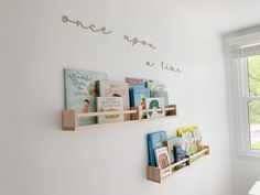 two wooden shelves with books on them in front of a window and a wall mounted book shelf