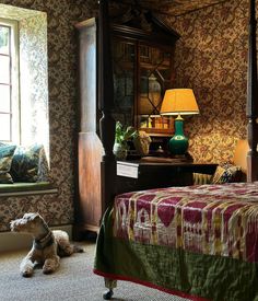 a dog laying on the floor next to a bed in a room with floral wallpaper