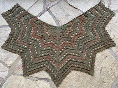 a crocheted shawl sitting on top of a stone floor next to a rock