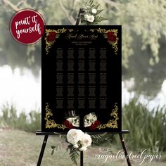 a black and gold wedding seating sign with roses on it, next to a river