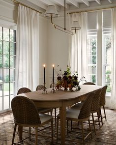 a dining room table with chairs and candles on it in front of large open windows