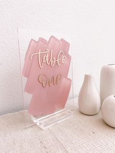 a table sign sitting on top of a table next to two vases and a white vase