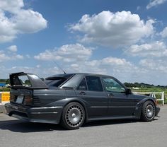 a black car parked in a parking lot next to a white fence and blue sky