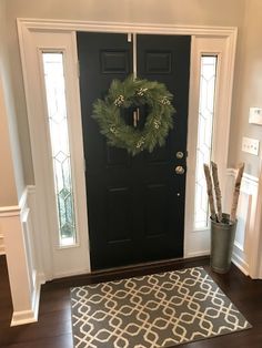 a black front door with a wreath on it and a rug in front of it