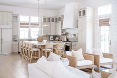 a white kitchen and living room are shown in this image, with the couches pulled back