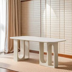 a white table sitting in front of a window next to a wooden floor and curtains