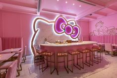 a pink hello kitty themed bar with gold stools and an illuminated hello kitty sign on the wall