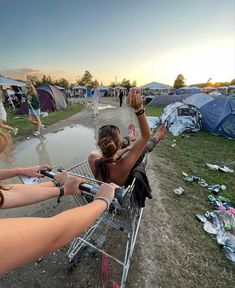 two women are sitting in a shopping cart at a camp site while the sun is setting