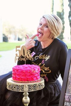 a woman sitting in front of a cake with the number 50 on it's top