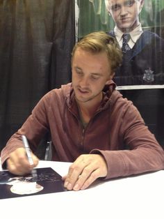 a man sitting at a table writing on a piece of paper with a pen in his hand