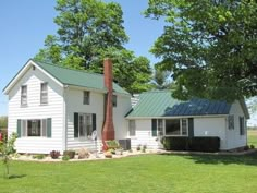 a white house with a green roof in the middle of a grassy area next to trees