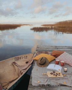 a hat and some food on a table near a boat in the water at sunset