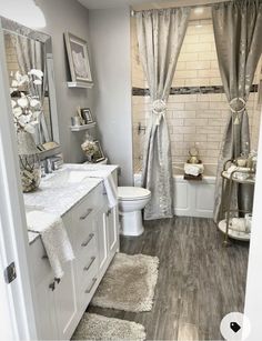 a bathroom with gray walls and white fixtures, including a toilet, sink, shower curtain, and rugs