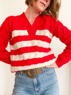 a woman wearing a red and white striped sweater with her hands on her hips, standing in front of a wall