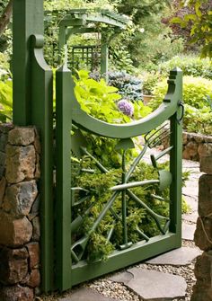 a green gate with plants growing in it and some rocks on the ground next to it