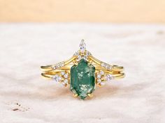 an emerald and diamond ring sitting on top of a white cloth covered surface with gold trimming