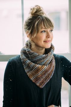 a woman standing in front of a window wearing a knitted scarf over her neck