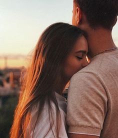 a man and woman standing next to each other with their arms around each other as the sun sets behind them