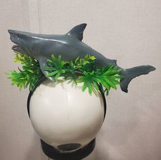 there is a fake shark on top of a vase with green plants in the bottom