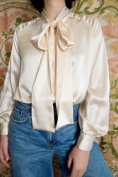 Beautiful silk pussybow blouse by Peter Hidalgo. This stunning wardrobe staple is made of a luxe, buttery silk. Scarf at neck can be tied in a variety of styles. Button front closures down front and at cuffs. One button is missing at cuff. The cuff still functions normally with only one button instead of two, and it could easily be replaced with any button in a similar shade. Priced to reflect missing button.  Size M-L. 20" pit to pit, 24" long. 100% silk. Y2K. Pussybow Blouse, Scarf Blouse, Silk Blouses, Phone Stuff, Cream Silk, Satin Blouse, Silk Blouse, Silk Scarf, Womens Clothing Tops