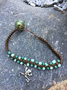 Macramed using a nylon beading cord in a rich brown color with small, sage-colored glass beads intertwined in the middle of the bracelet. The cheerful silver-toned hopping frog charm is added off center and loosely dangles from the strong brown cord. The bracelet ends join with a cord loop and a beautiful large sage and brown "kiln-fired glaze" look 1/2-inch bead that is securely tied to the other end.  Perfect shabby chic bracelet for casual or dress casual days or nights! Green Macrame Jewelry With Beads, Green Macrame Jewelry With Round Beads, Adjustable Green Beaded Braided Bracelet, Adjustable Green Braided Beaded Bracelets, Bracelet Ends, Beading Cord, Bracelet Craft Diy, Chic Bracelet, Bracelet Crafts