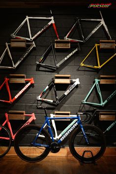 several different colored bikes are on display in front of a wall with wooden crates and shelves