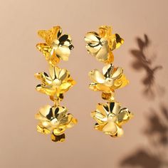 Introduce a touch of vintage charm to your look with our Golden Petal Earrings. These elegant drop earrings feature a trio of delicate flowers, meticulously crafted to bring a whimsical yet sophisticated accent to your attire. The golden hue adds a warm glow, making these earrings a versatile addition to both casual and formal outfits. Key Features: - Vintage Floral Design: Three-dimensional petals create a blooming bouquet that dangles gracefully. - Golden Finish: The earrings are plated in a rich gold tone for an opulent look. - Lightweight and Comfortable: Designed for all-day wear without compromising style. - Versatile Accessory: Perfect for adding a pop of vintage flair to any ensemble. - Ideal Gifting: A beautiful choice for gifting on special occasions or as a self-treat. Ordering Metal Flower Earrings With Flower Charm, Elegant Clip-on Earrings With Flower Charm, Elegant Metal Earrings With Flower Charm, Elegant Metal Flower Earrings, Elegant Metal Flower Charm Earrings, Metal Flower Charm Drop Earrings, Metal Drop Earrings With Flower Charm, Gold Dangle Earrings With Flower Decoration, Gold Metal Flower Charm Earrings