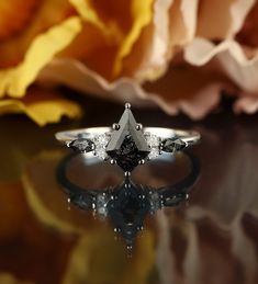 a diamond ring sitting on top of a table next to a rose flower with petals in the background