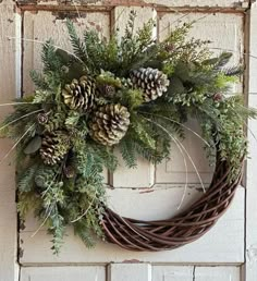 a wreath with pine cones and greenery hanging on a door