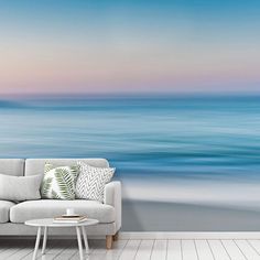 a living room with a couch, coffee table and ocean wall mural on the wall