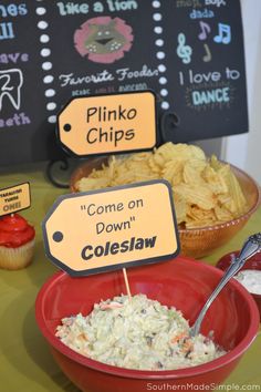 a bowl of coleslaw and cupcakes on a table with signs that read pinko chips come on down coleslaw