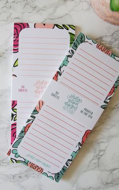 two lined notepads sitting on top of a marble counter next to an apple